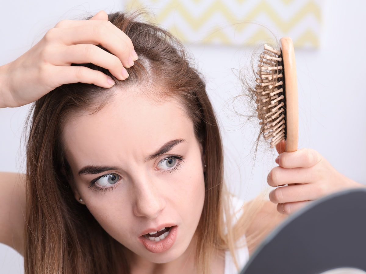 Perceber queda de cabelo dicas. Na foto a mulher está observando uma escova de cabelo cheia de fios