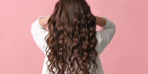 Cuidados essenciais cabelo ondulado. Foto mulher com cabelo ondulado comprido em um fundo rosa.