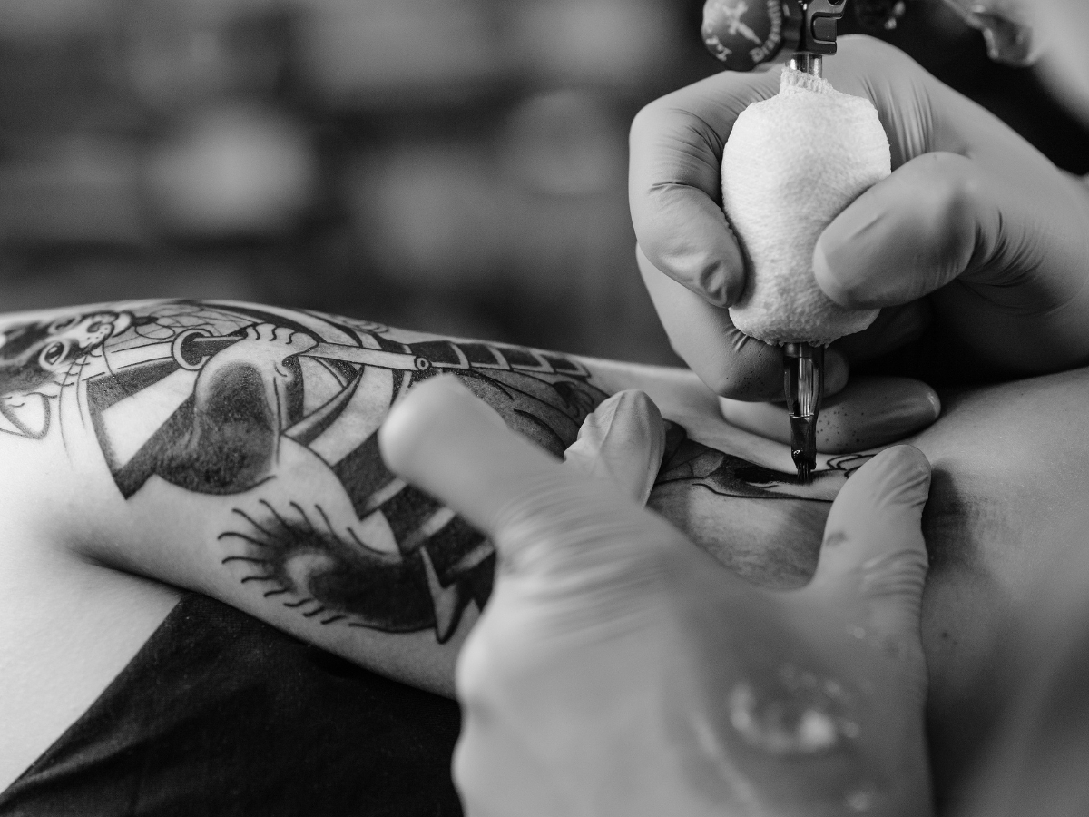 Cuidados essenciais com nova tatuagem. A foto mostra um braço sendo tatuado