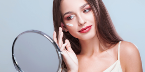 Dermomake. Foto mulher branca em frente ao espelho usando maquiagem em creme no rosto
