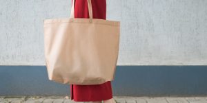 Estilos de Bolsas para complementar looks. Foto traz uma bolsa sacola de cor bege e mulher segurando -a com look vermelho