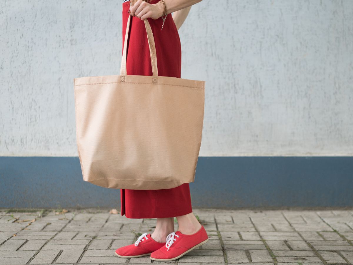Estilos de Bolsas para complementar looks. Foto traz uma bolsa sacola de cor bege e mulher segurando -a com look vermelho