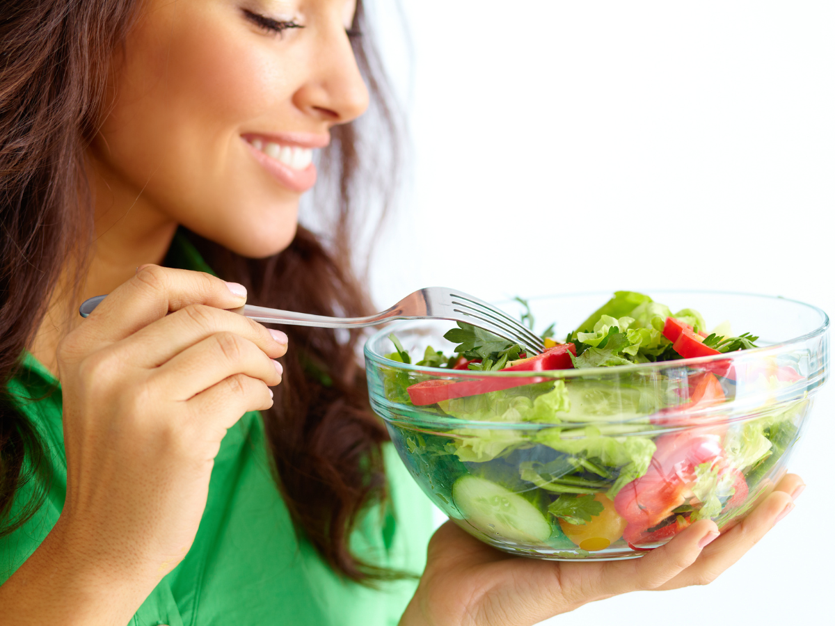 Impacto da alimentação na pele. Foto possui uma mulher branca com camiseta verde e um pote de salada