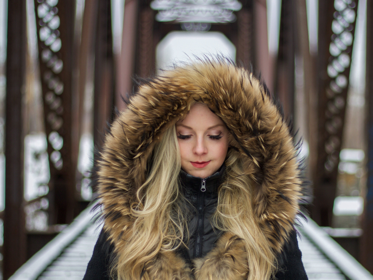 Manter os fios saudáveis no inverno. Foto mostra uma mulher com toca de pele protegendo os cabelos loiros do frio.