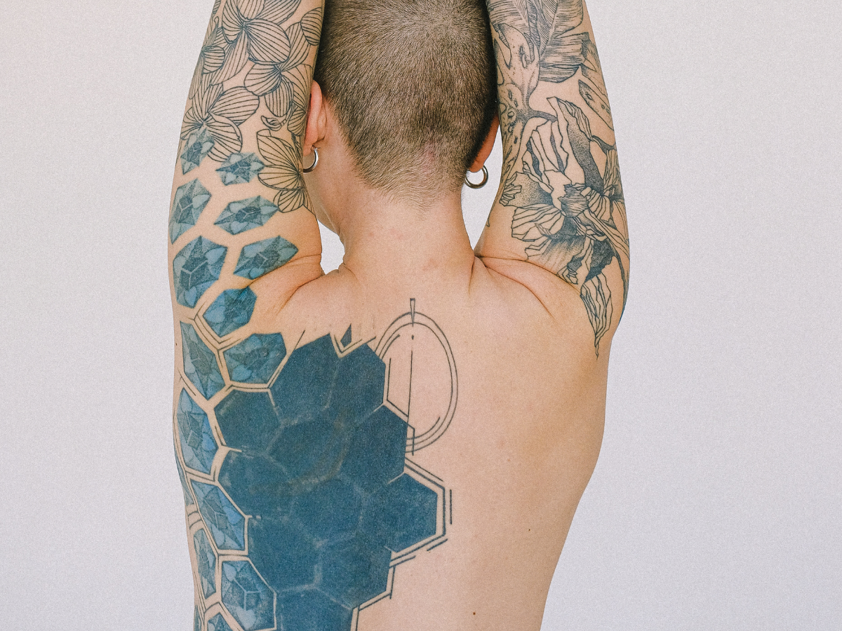 Tatuagens para cobrir outras. Foto mostra uma mulher de costas com as costas tatuadas de um desenho abstrato todo em preto.