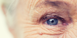Células Zumbis no envelhecimento da pele. Foto aparece um rosto de idoso com rugas aparentes e de olho azul.