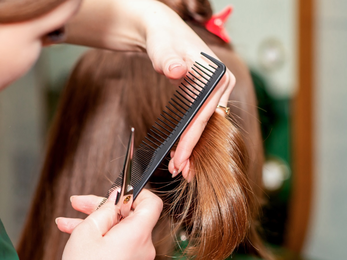 Corte de cabelo ideais para cada tipo de rosto. Foto mostra um cabelo castanho sendo cortado. Pente preto e tesoura prata.