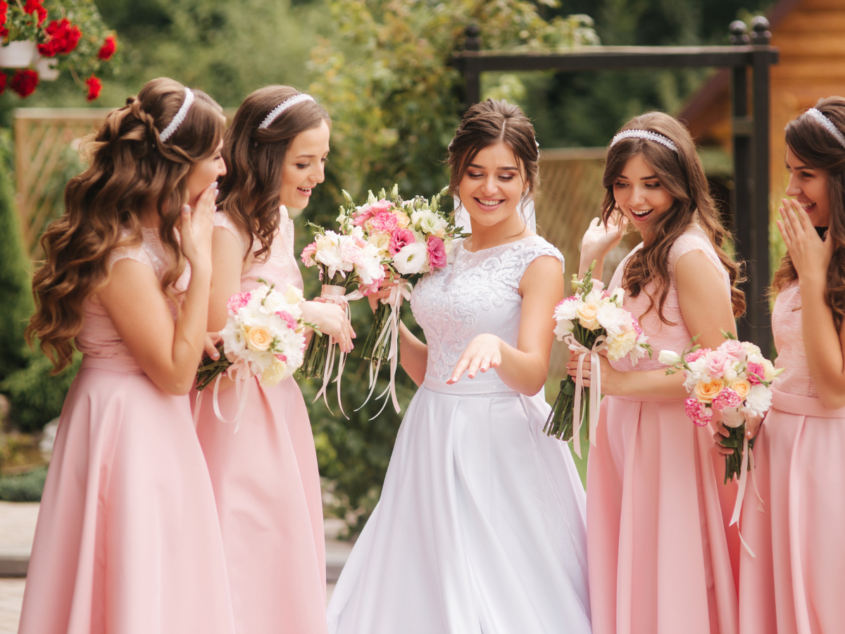 Ideias de looks para madrinhas de casamento. Foto noiva de branco com as madrinhas ao redor com vestido cor de rosa.