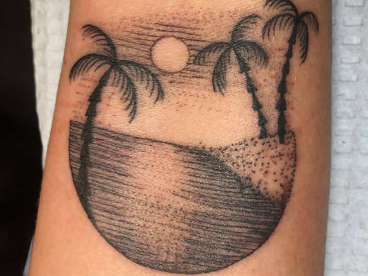 Tatuagens de mar e praia. Foto mostra uma tatuagem com palmeiras, o mar e um pôr do sol ao fundo