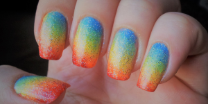 Unhas decoradas com as cores do arco-íris. Foto unhas com os dedos coloridos com vermelho, amarelo, verde e azul em formato degradê.