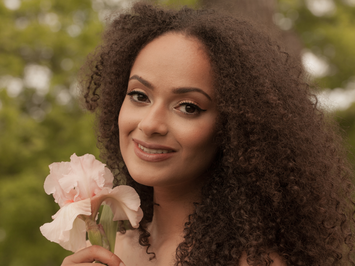 Cabelo crespo mentiras que já te contaram. Foto mostra uma mulher negra com cabelo crespo segurando uma flor rosa na mão.