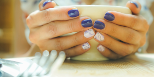 Unhas color block tendência. Foto mostra mãos pintadas de branco e azul segurando uma xícara.
