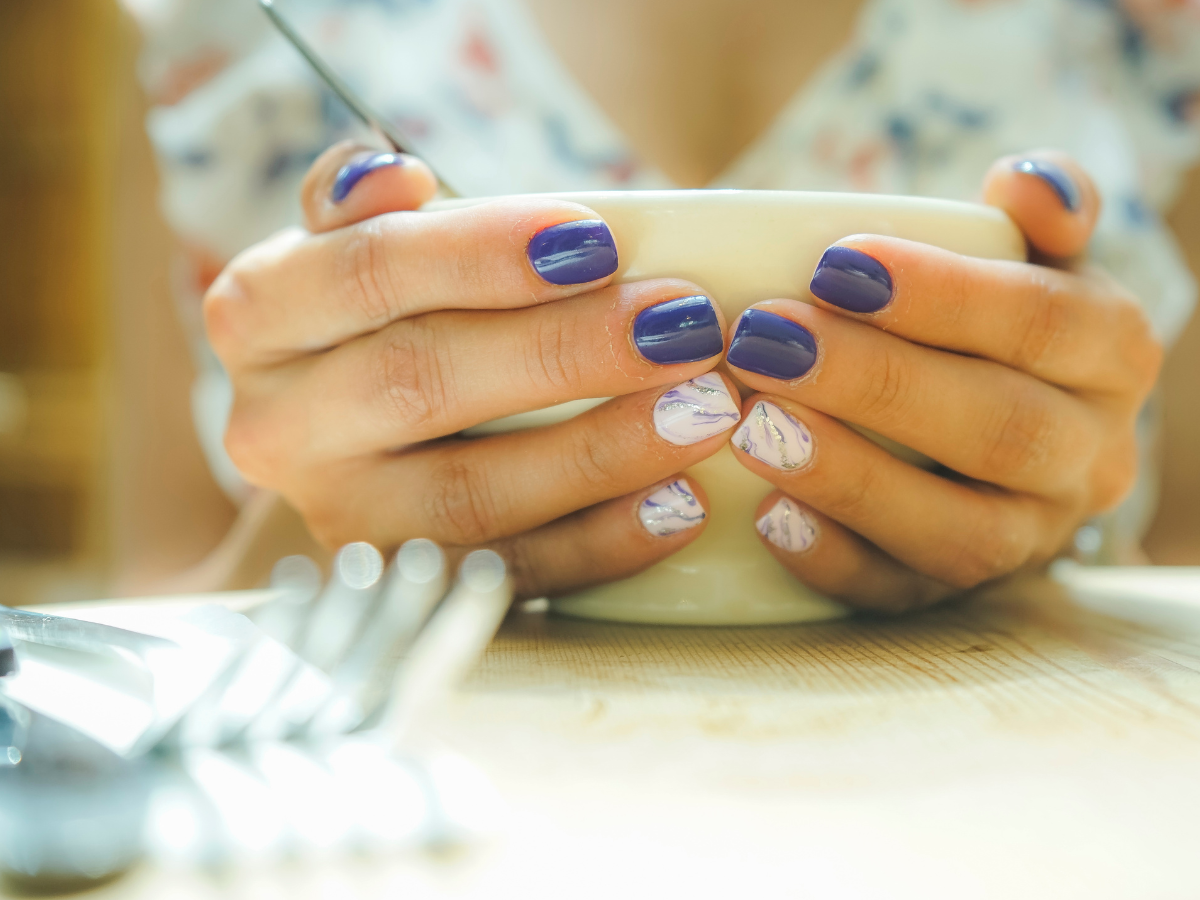 Unhas color block tendência. Foto mostra mãos pintadas de branco e azul segurando uma xícara. 