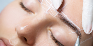 Risco na sobrancelha. Foto mostra uma mulher com o rosto riscado de branco e fazendo um procedimento na sobrancelha.