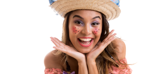 Maquiagem para festa junina. Foto mostra mulher sorrindo com sardinhas desenhadas na bochecha e chapéu junino