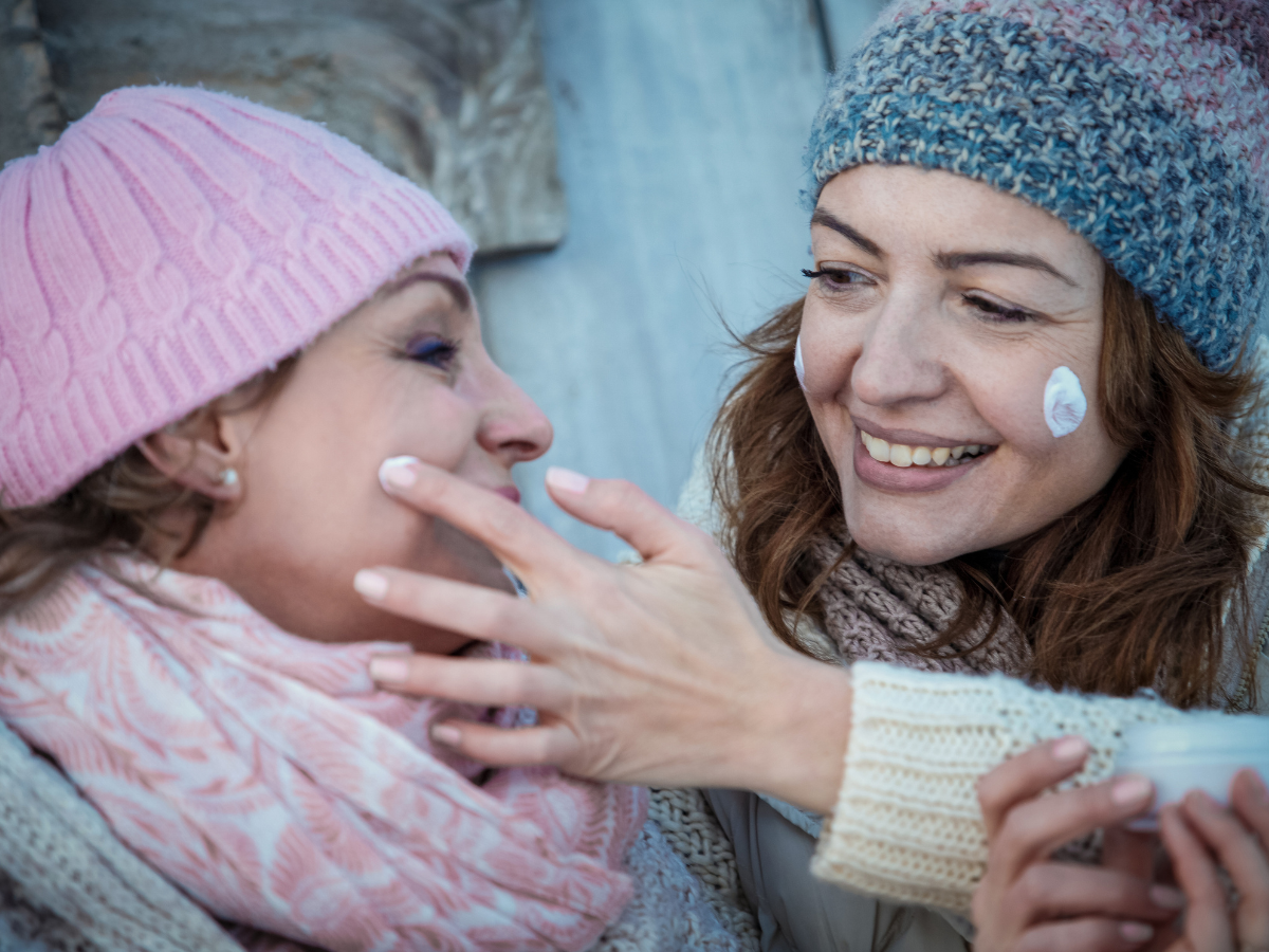 Pele e lábios hidratados no inverno. Foto aparece duas mulheres sorrindo passando produtos na pele.