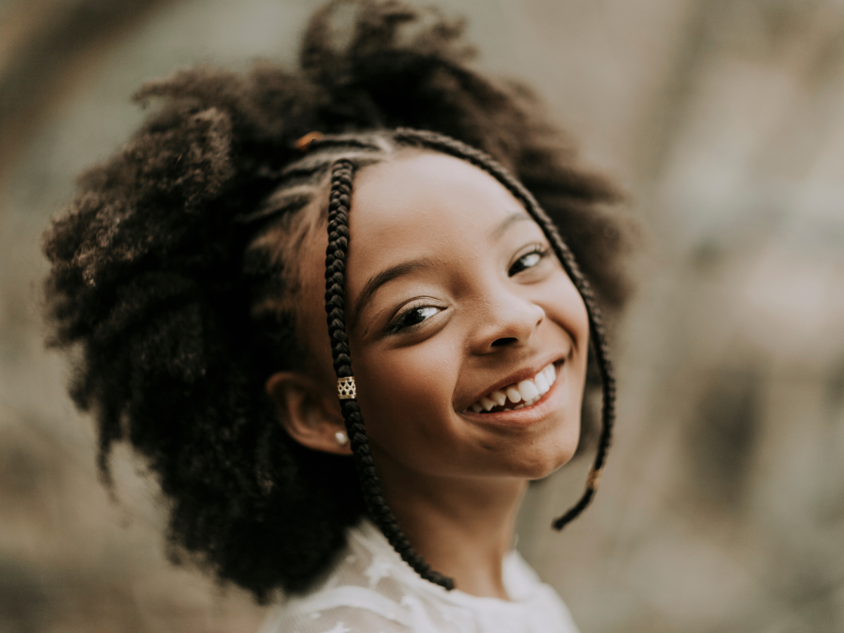 Penteado infantil simples. Foto mostra menina criança de pele negra com tranças no caelo e sorrindo