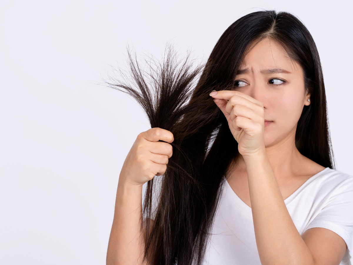 Como identificar que o cabelo está danificado. Foto mostra mulher olhando os fios do cabelo com cara de preocupada