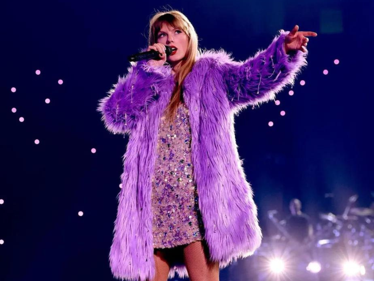 Taylor Swift vestindo uma roupa peluda roxa e cantando.