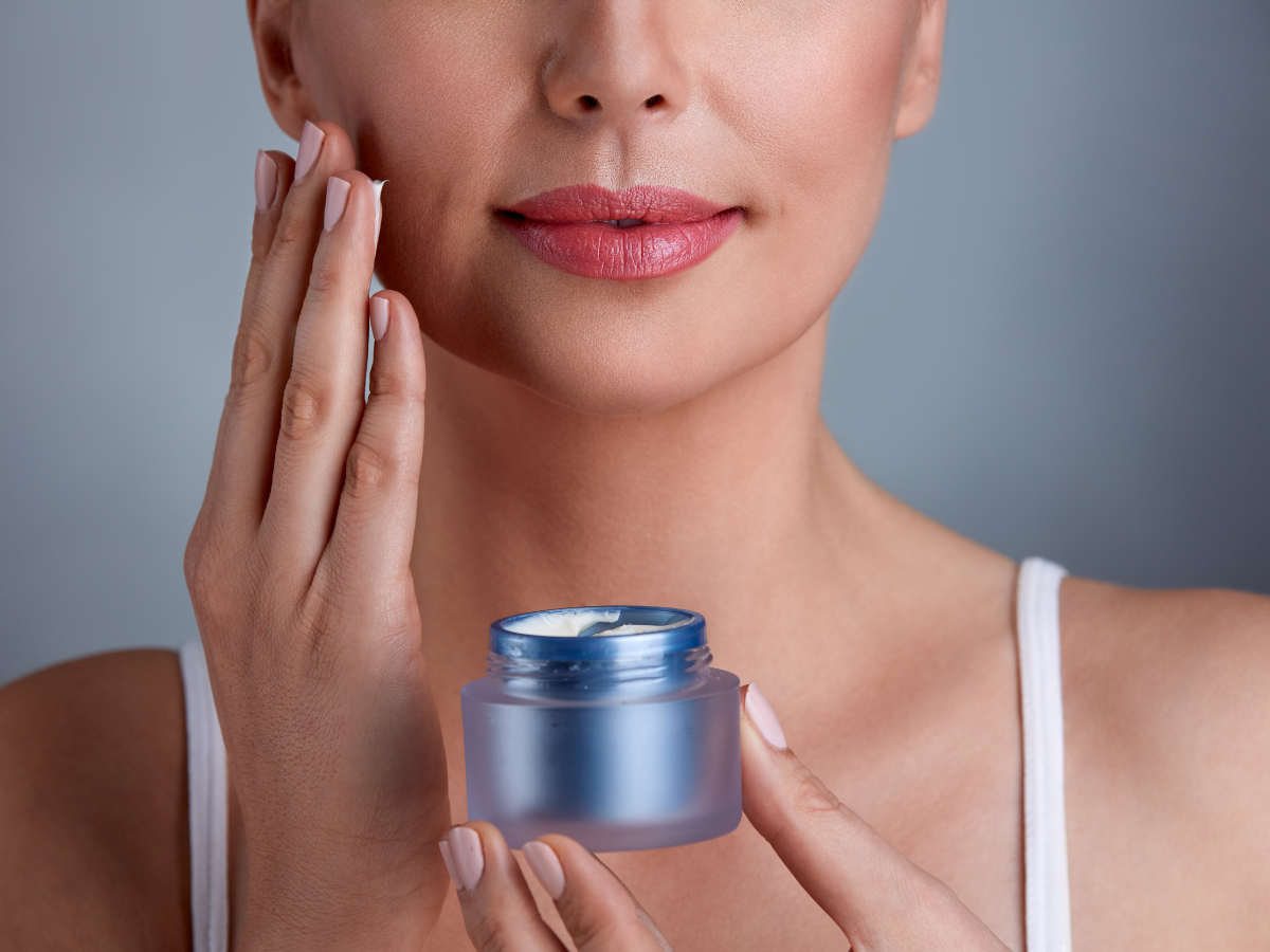Skincare para Pele Seca. Foto mostra mulher aplicando produto de embalagem azul sobre o rosto.